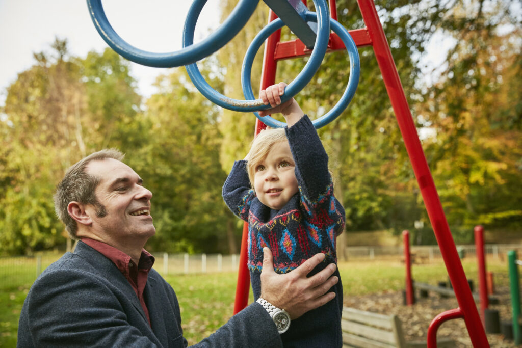 Father helping daughter on monkey bars in playground